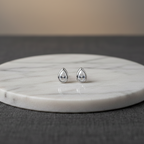 Teardrop-shaped earrings on a marble stand with a neutral background